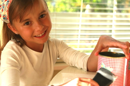 Little girl applying Mod Podge to the can sealing the decorative paper that has been applied to the can. 